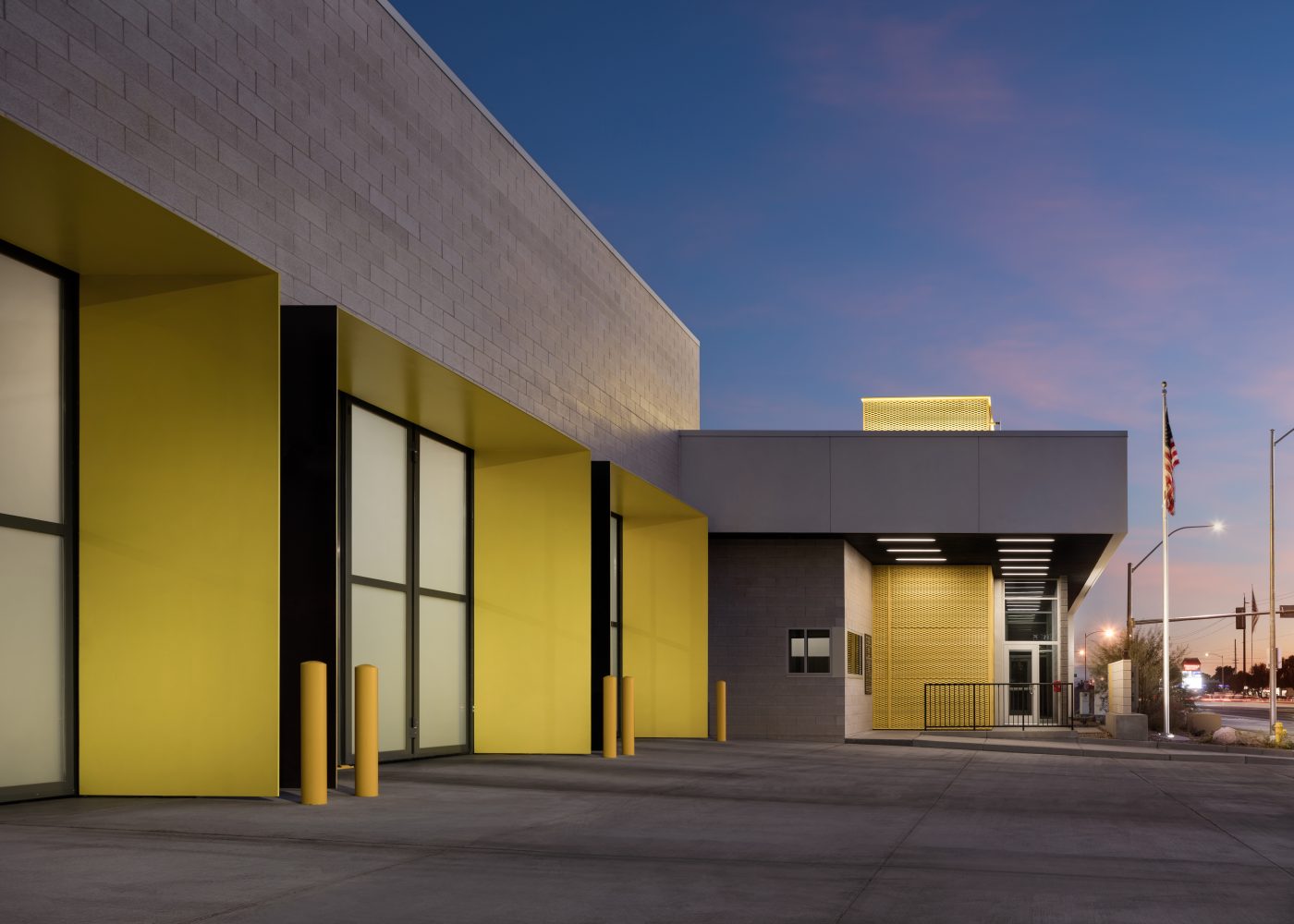 Twilight view of the exterior of Clark County Fire Station 61 in Las Vegas, NV. The three large apparatus bay doors are to the left. The main public entrance is straight ahead. The captain's office windows are also visible to the left of the main entrance.