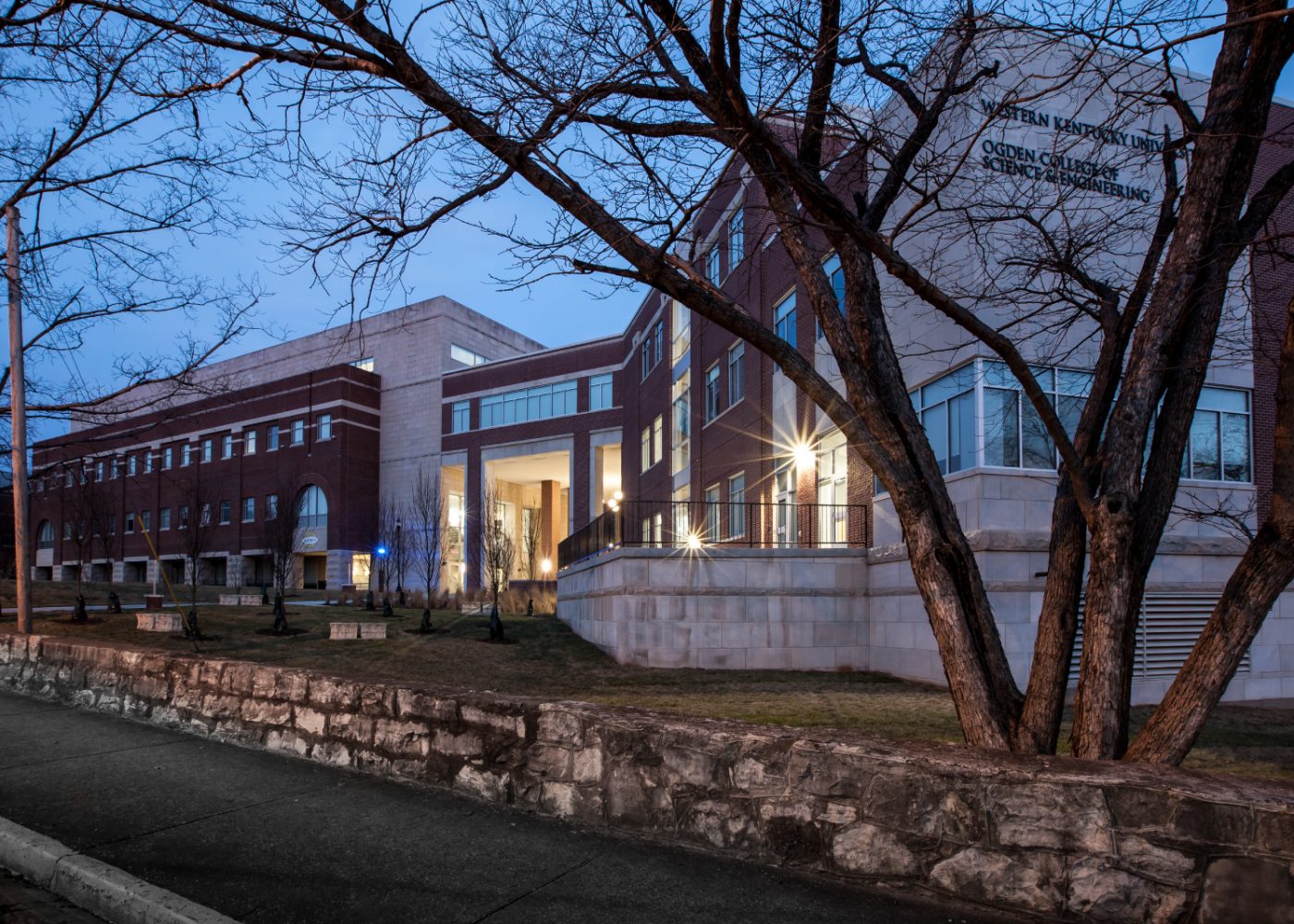A brick building is lit up at dusk.|higher education exterior building|higher education building exterior nighttime|higher education students learning science lab|higher education students learning science lab|higher education hallway student collaboration|higher education building lecture auditorium classroom|higher education building interior design hallway|higher education outdoor building exterior||||||||||||||||